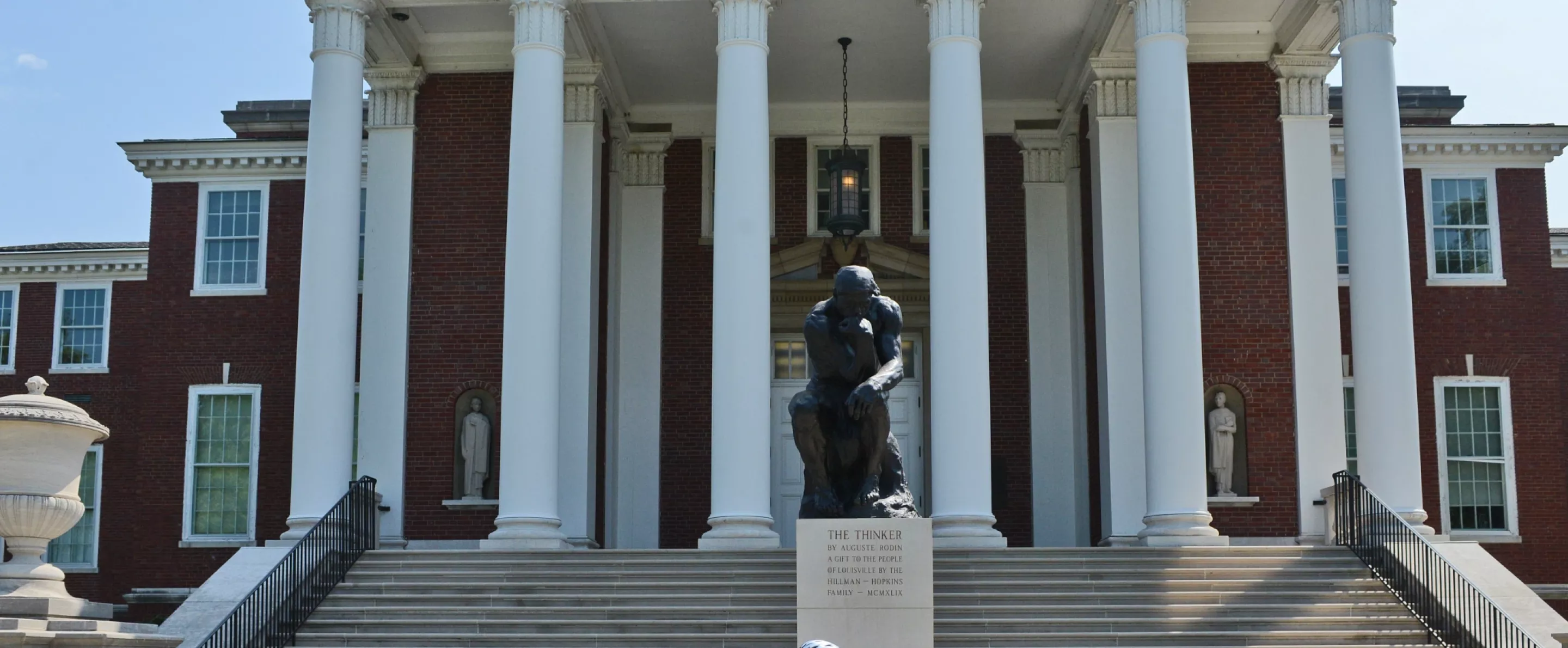 Student biking past the Thinker in front of Grawemeyer Hall