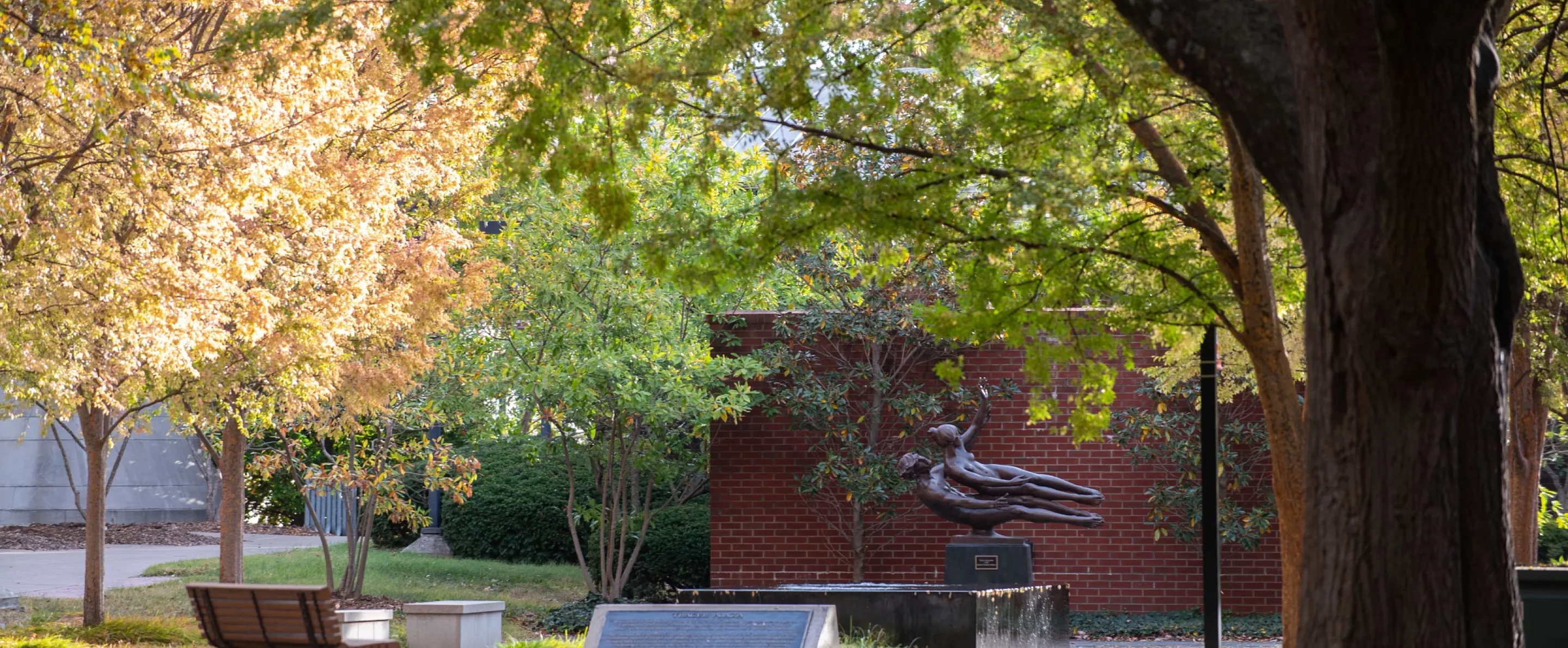 Small courtyard surrounded by trees with bench and statue of male and female.