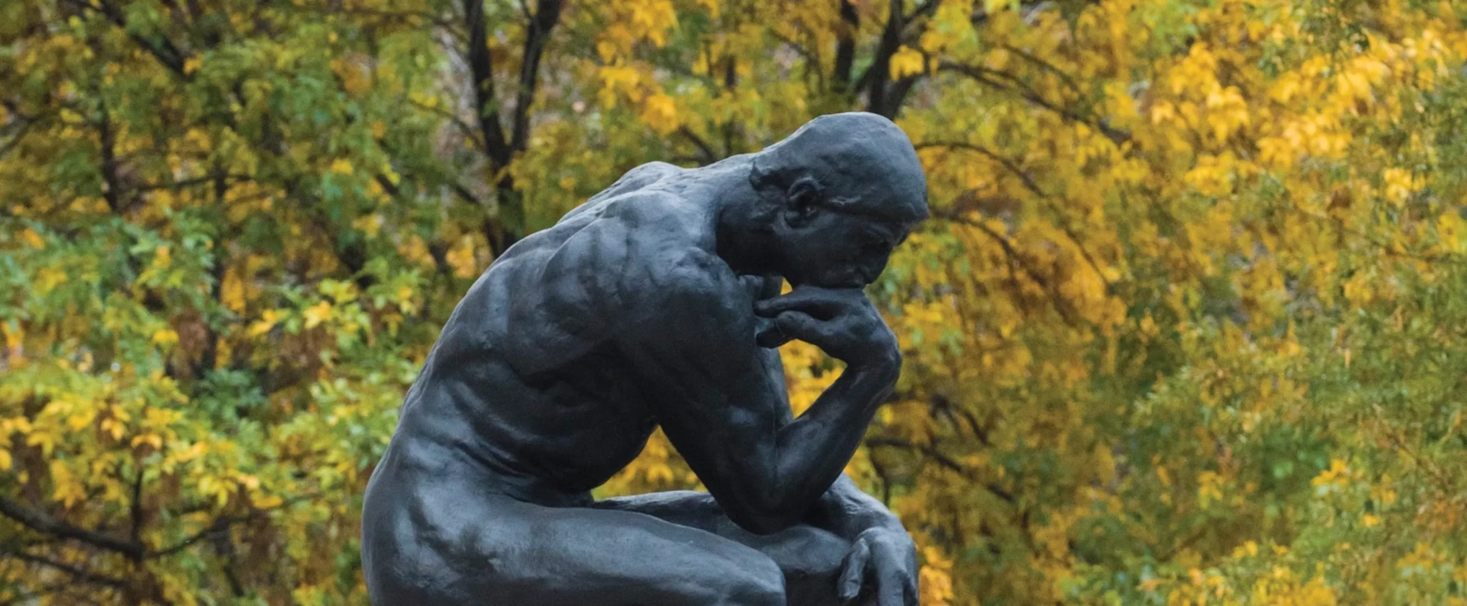 The Thinker statue in front of yellow and green foliage.