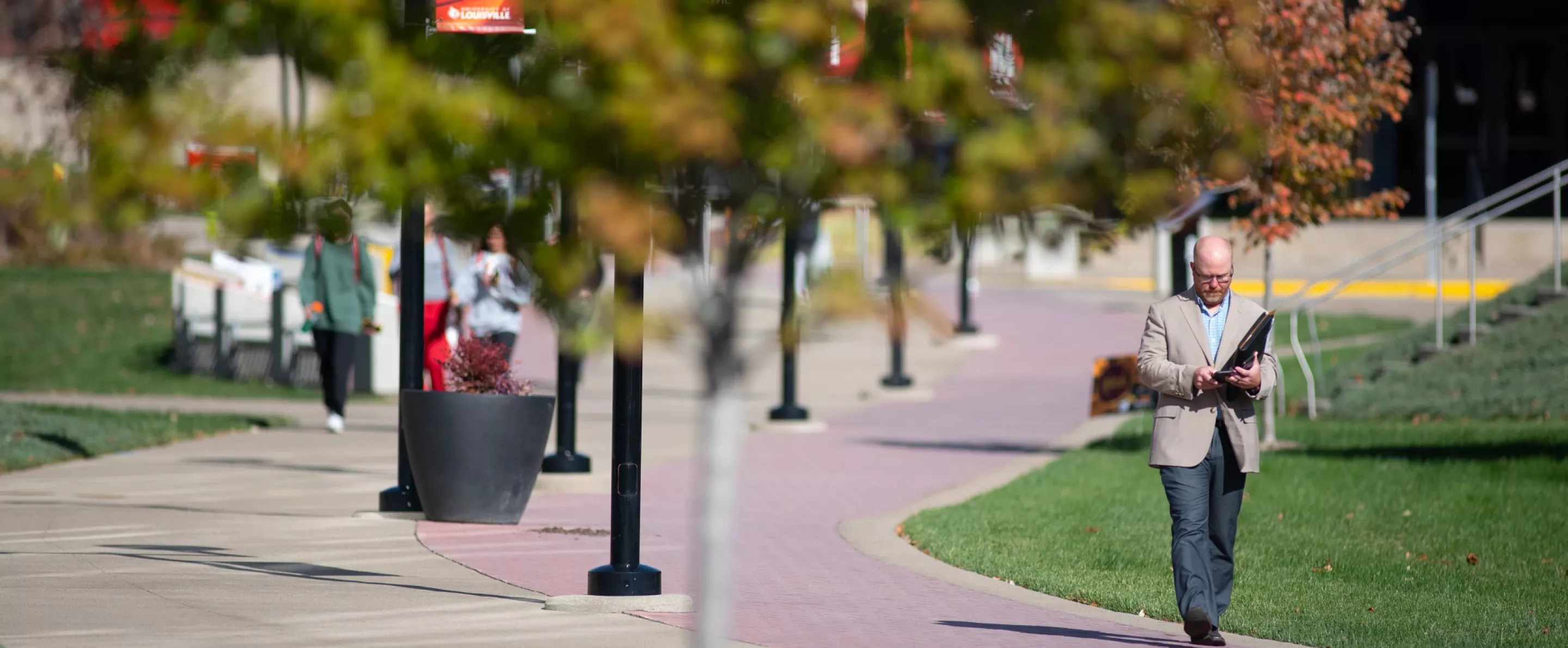 People walking along brick and sidewalk next to the Belknap Academics Building in the fall.