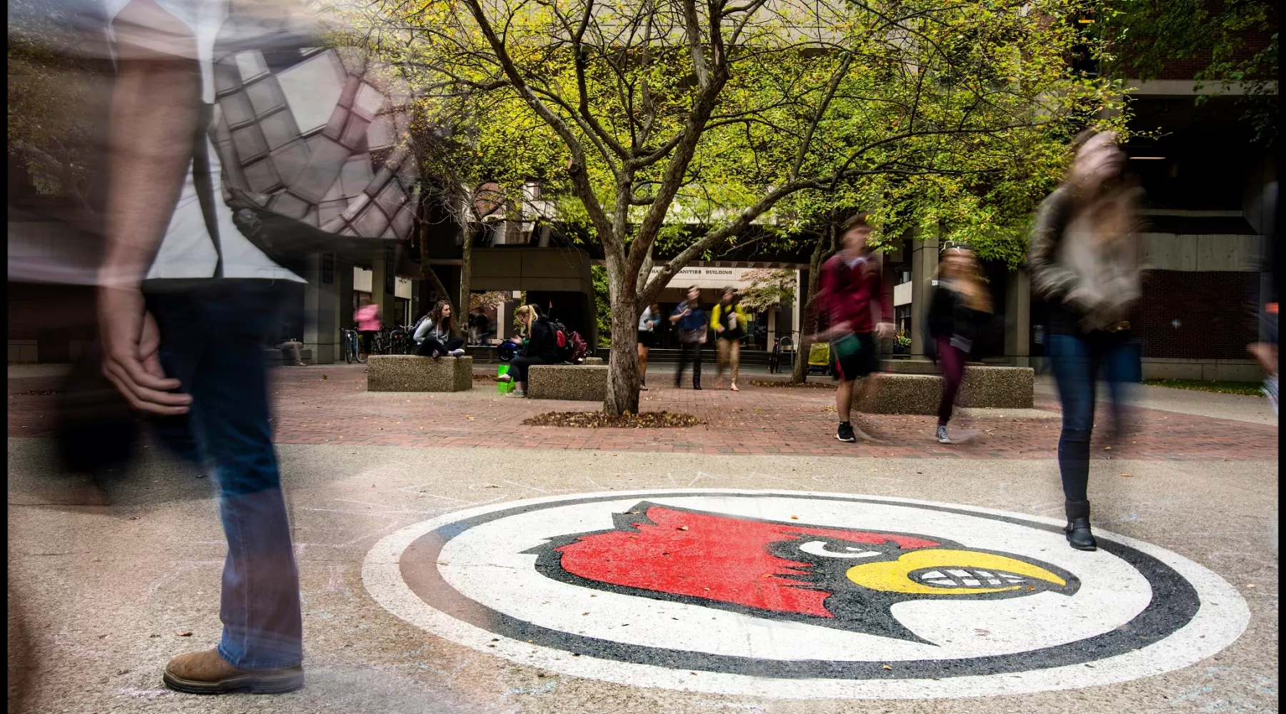 Blur of students walking by Cardinal Bird in front of Humanities