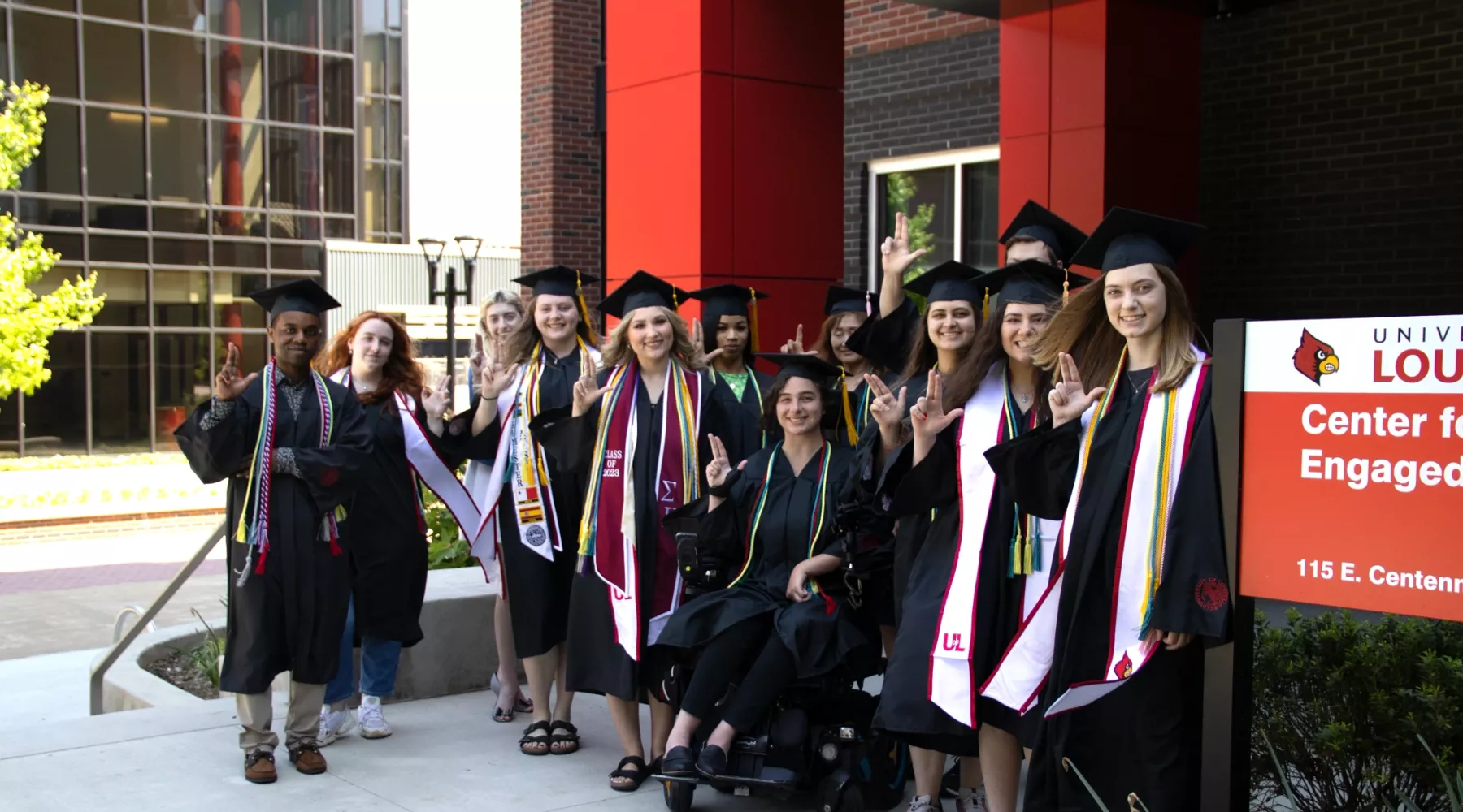 Group of students in caps and gowns posing by the Center for Engaged Learning's entrance sign