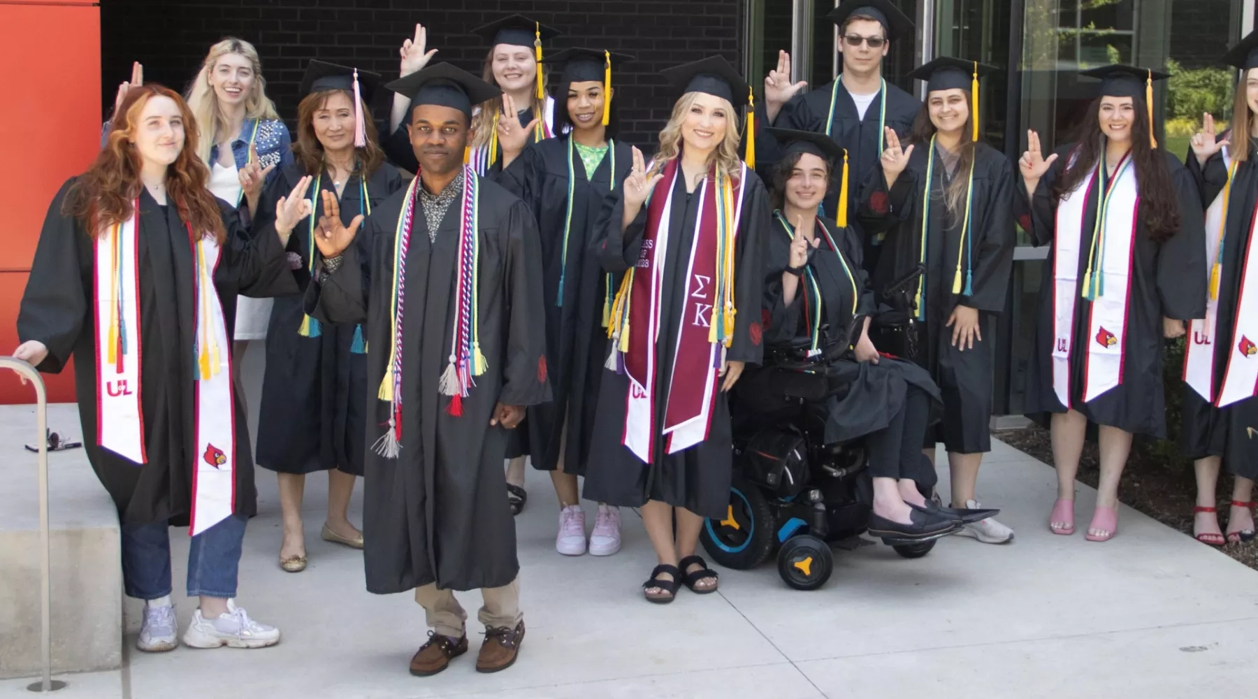 A group of graduates in caps and gowns giving the L hand sign