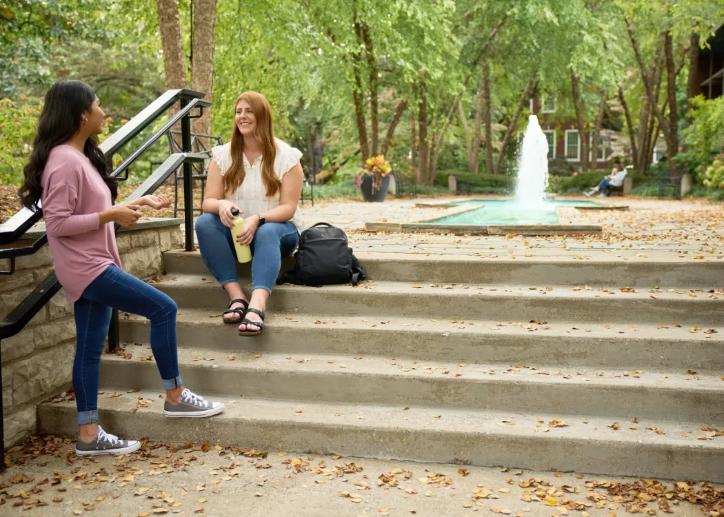 Two students talking on the stairs of the fountain area.