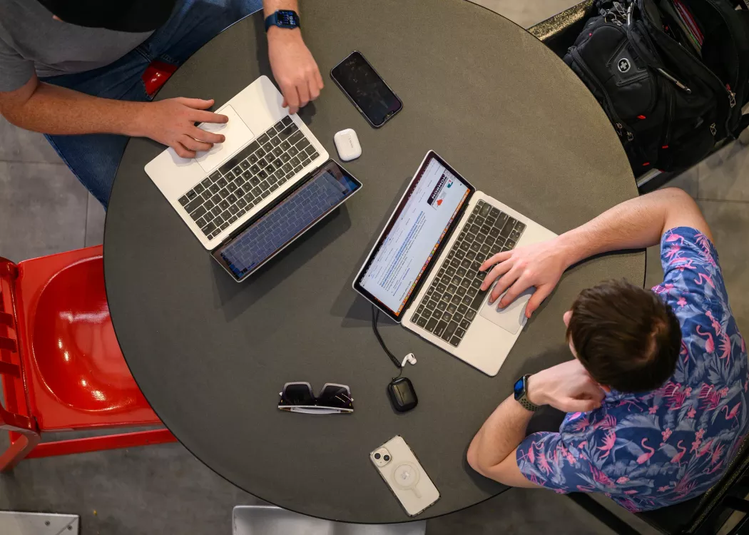 Aerial view of students working on laptops at round table.