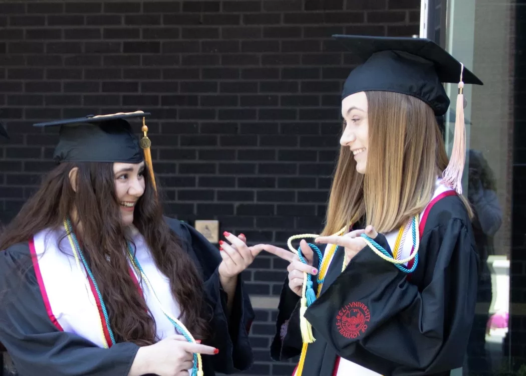 Two students in caps and gowns pointing at each other
