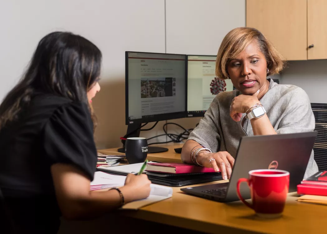 Two female employees seated during a meeting discussing content on screen of laptop