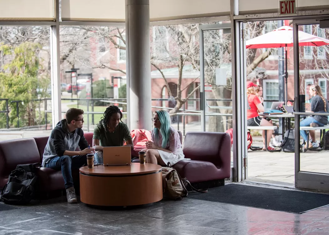 Three fine art students working together in the lobby of Schneider Hall