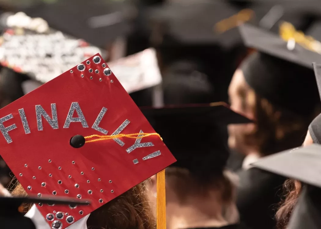 University of Louisville student at graduation with the word finally decorated on their hat.