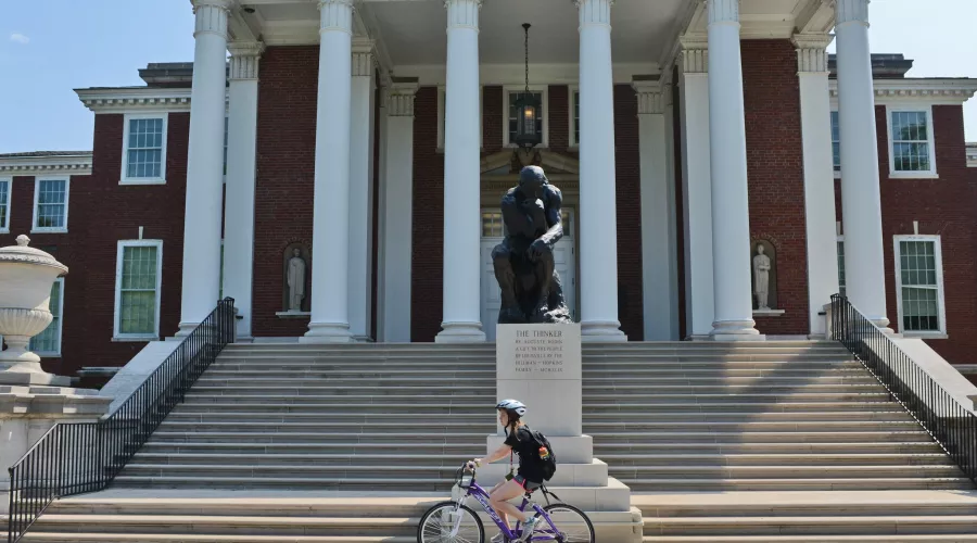 Student biking past the Thinker in front of Grawemeyer Hall