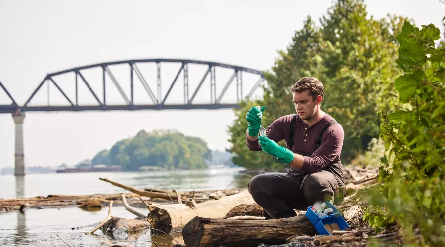 Sam Kessler is testing the water at the Ohio river as he sits close to the edge of the river to retrieve and test the sample.