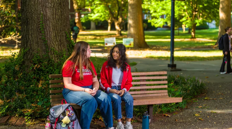 Two students talking on a bench on Belknap Campus