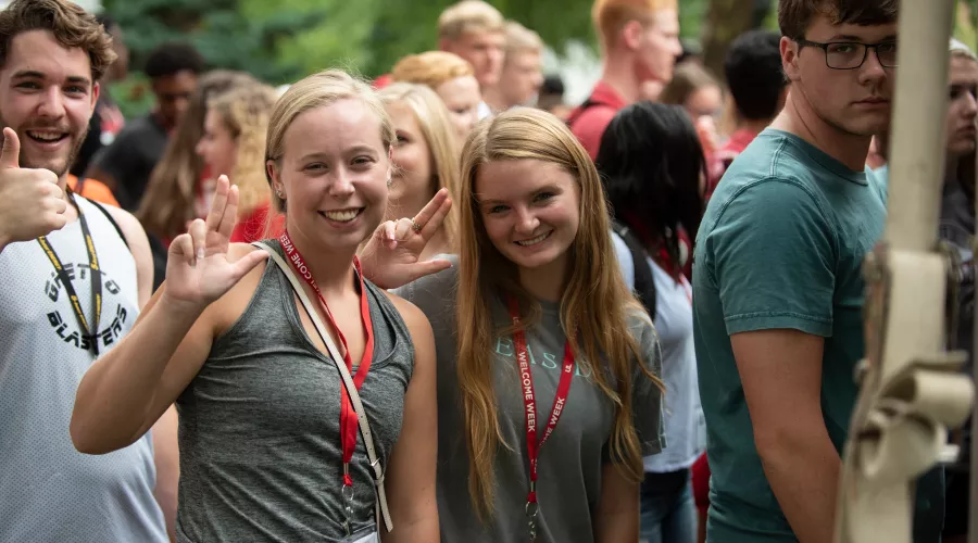 Three students at Orientation smiling towards the camera and throwing up their L's
